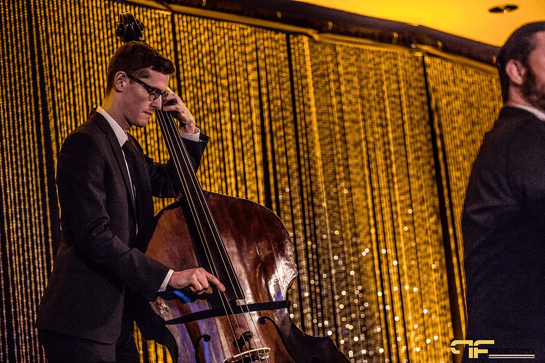 Upright bassist playing in front of a gold sequin-strand stage curtain
