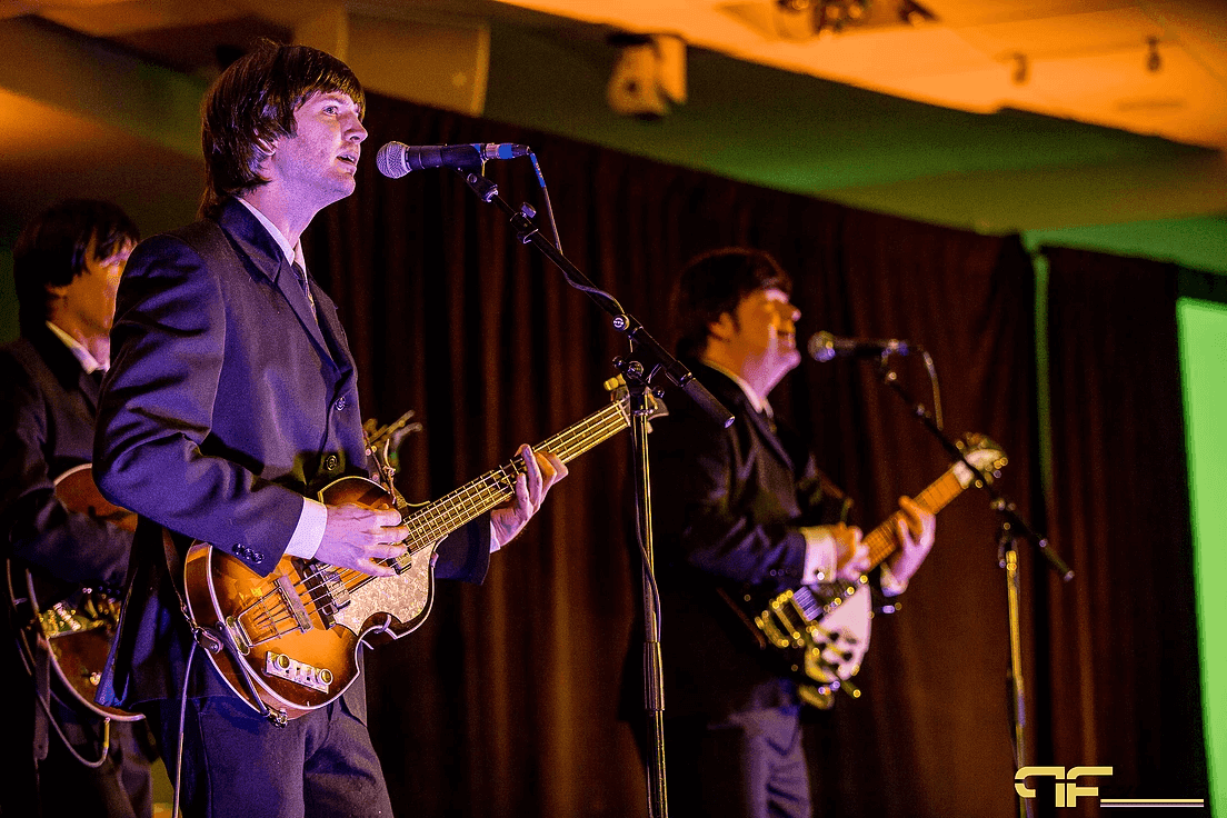 Tribute band bassist and guitarist singing into boom-stand mics on stage