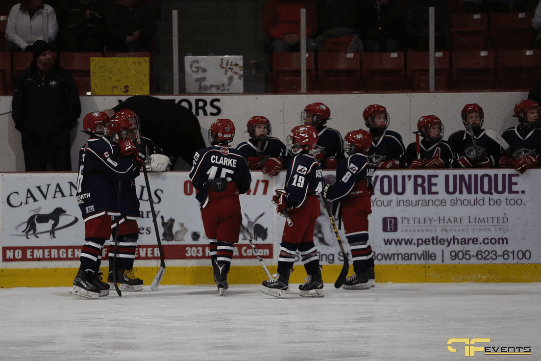 Players in red helmets gather at the bench in front of the rink boards