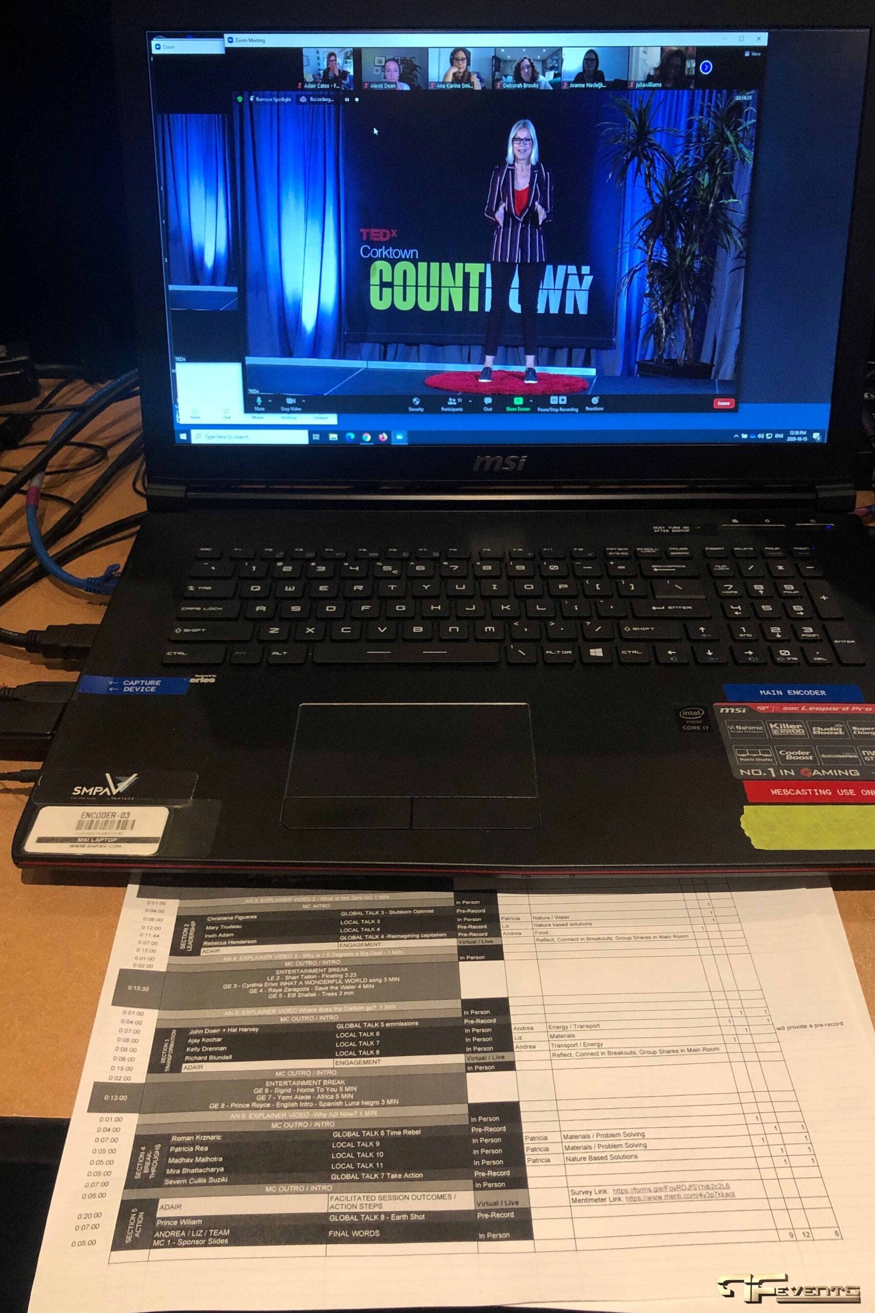 Webcast encoder laptop showing a remote talk over Zoom beside a run-of-show