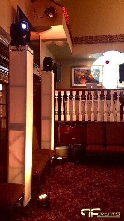 Moving head on a white-wrapped totem beside speakers and a balcony DJ booth