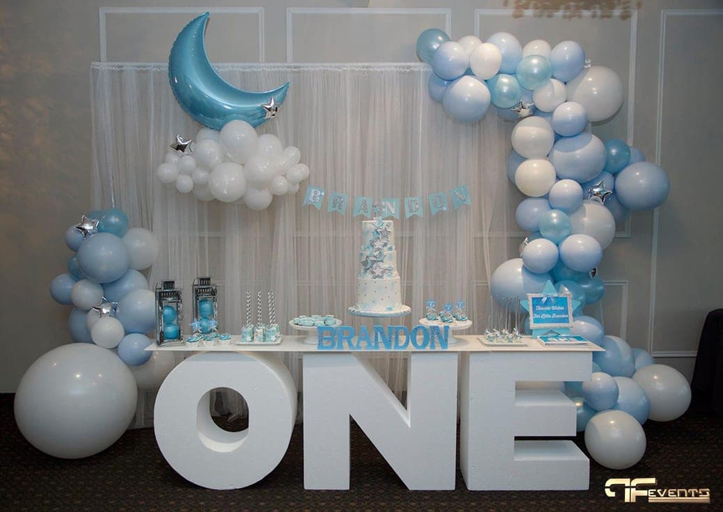 Dessert table on giant white “ONE” letters, framed by blue and white balloon garland
