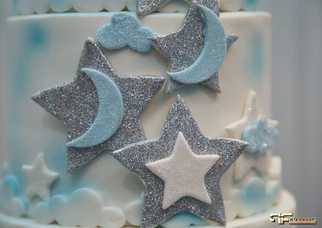 Glitter stars, moons and clouds on the side of a white and blue cake