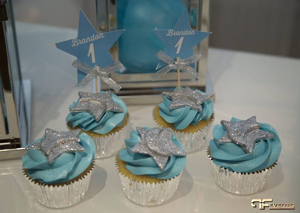 Cupcakes with blue frosting and star picks beside a mirrored lantern