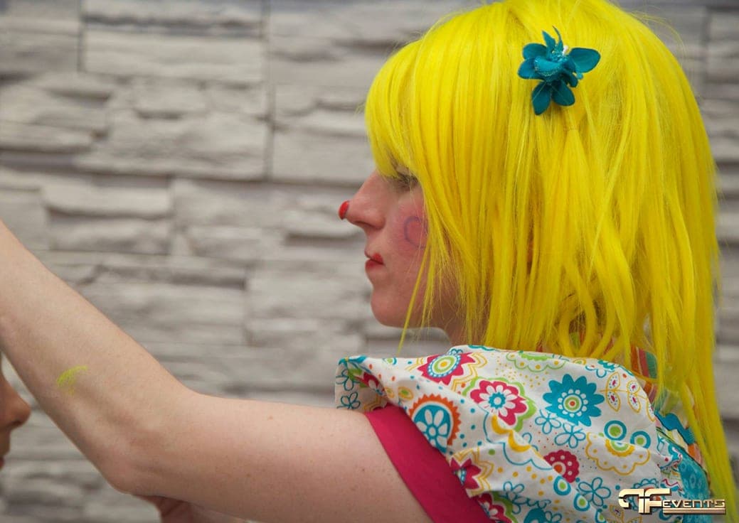 Clown entertainer in a yellow wig face-painting a guest's arm