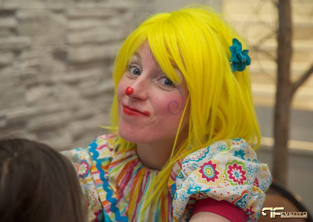 Clown entertainer with yellow wig and red nose smiling at a children's party