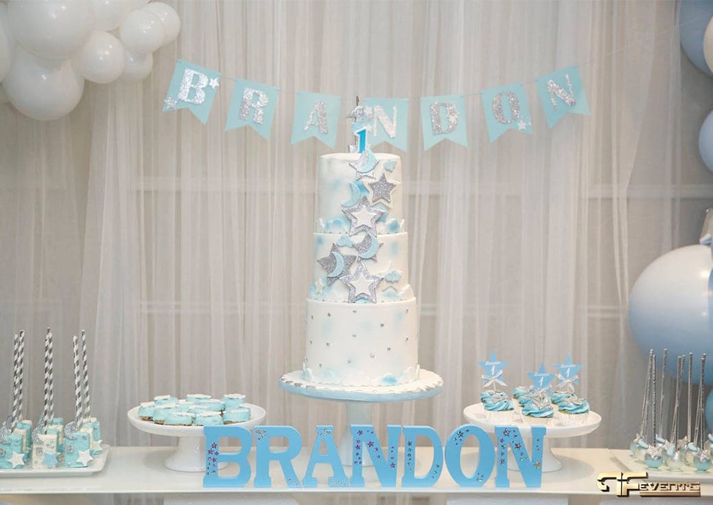 Star and moon birthday cake behind blue name letters on the dessert table