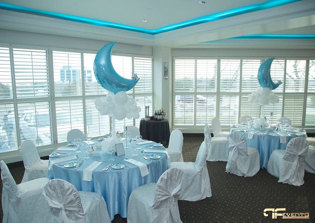 Banquet room with baby-blue linens, white chair covers and moon balloon centrepieces