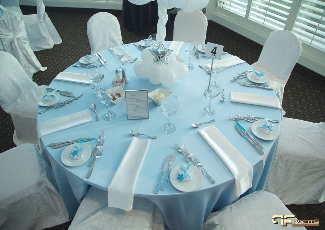 Table setting with blue satin cloth, white napkins, favours and a balloon cloud centrepiece