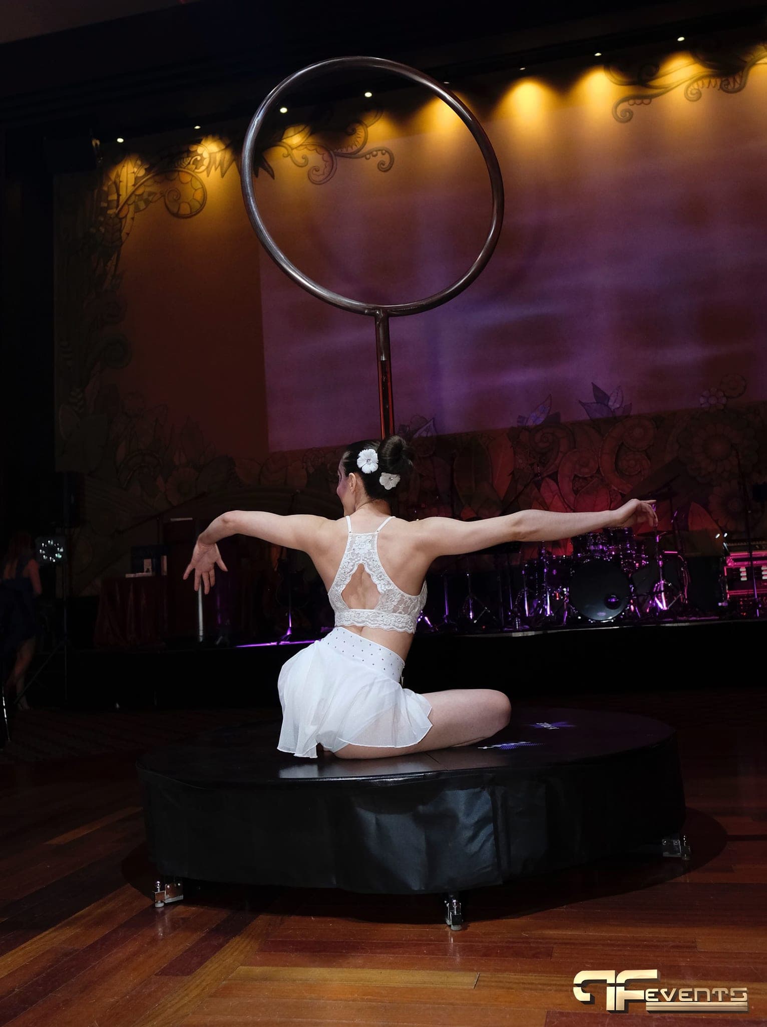Lyra performer on a round black riser before a purple-lit stage wall