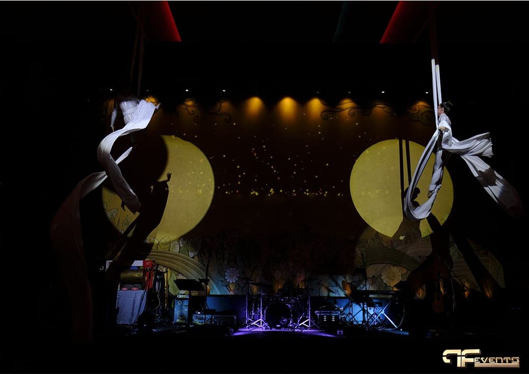 White-silk aerial duo silhouetted against twin yellow circles and a starfield