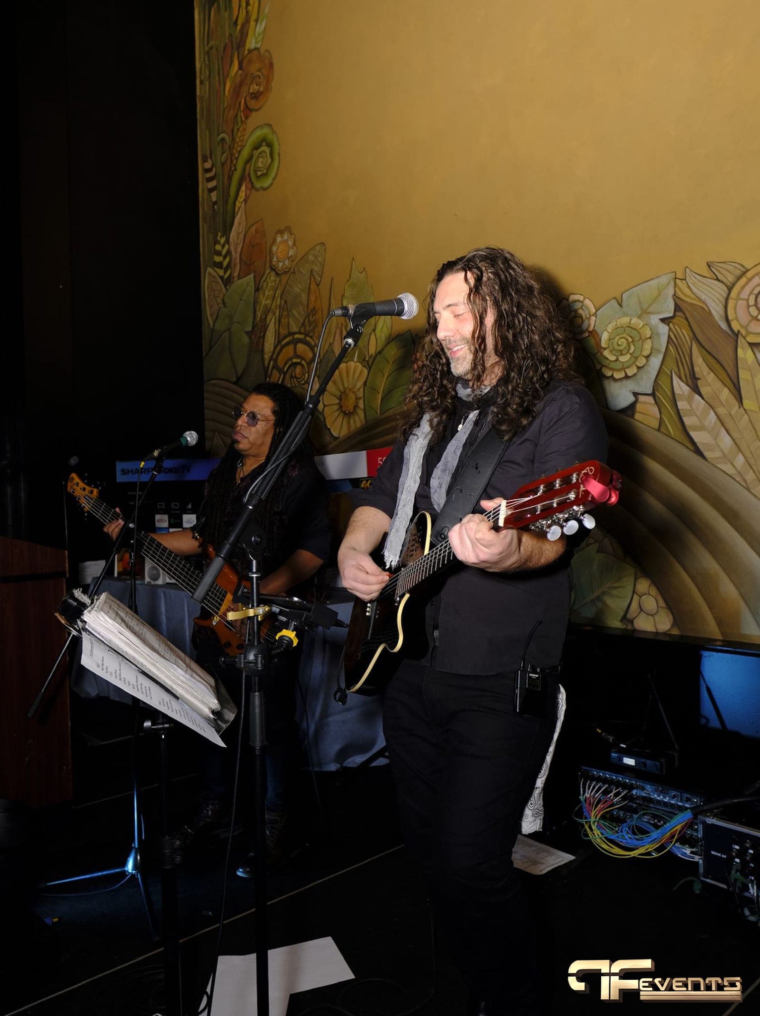 Guitarist and bassist singing on stage in front of the floral mural