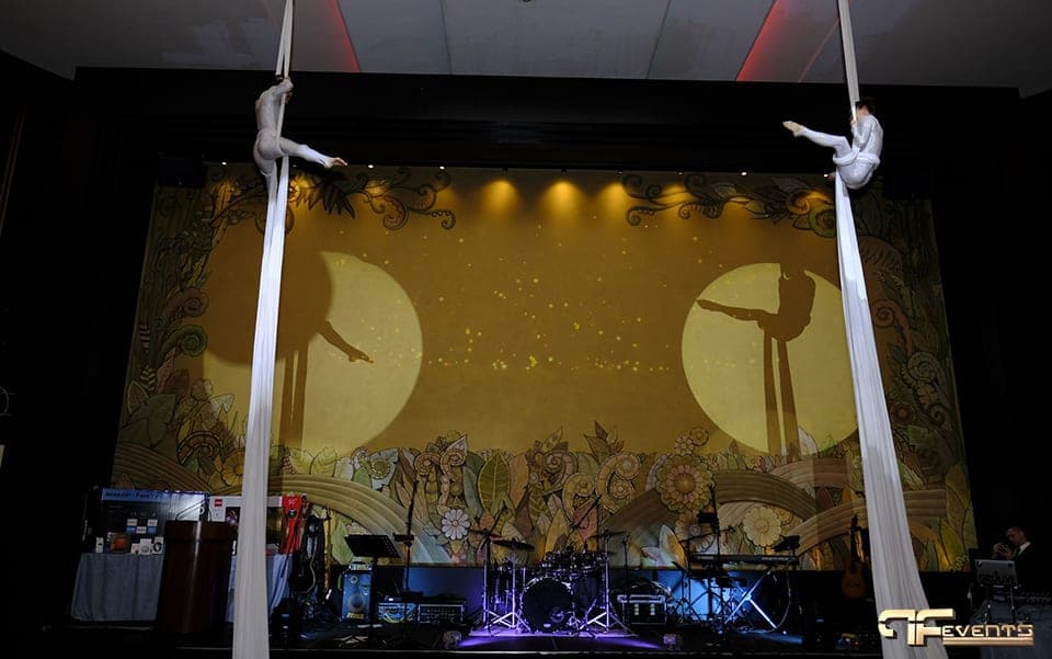 Aerialists climbing white silks either side of the moon-lit stage wall