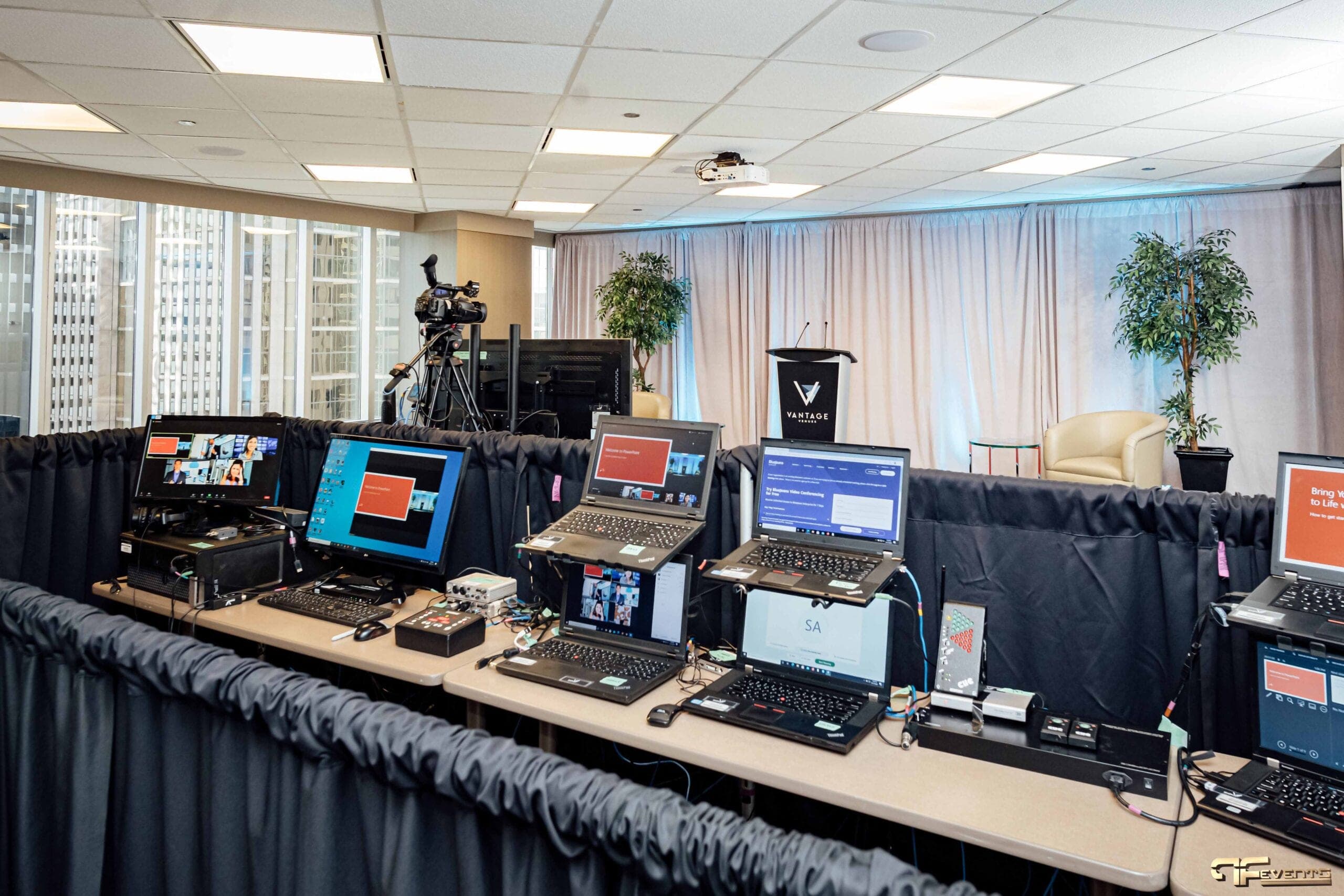 Laptop and monitor bank behind pipe-and-drape facing the studio stage