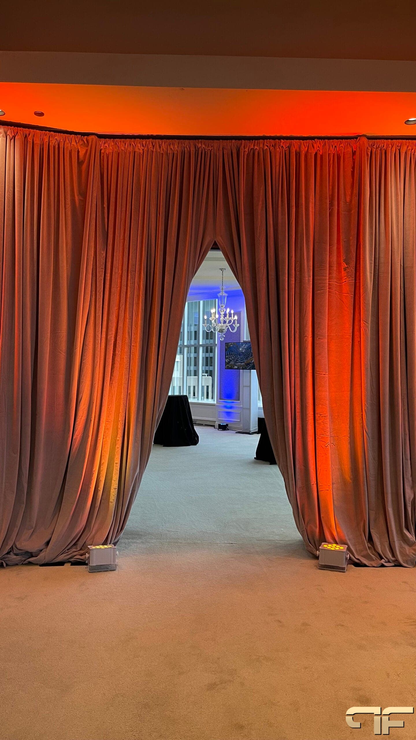Draped archway washed orange by uplights, opening onto a blue-lit room with chandelier