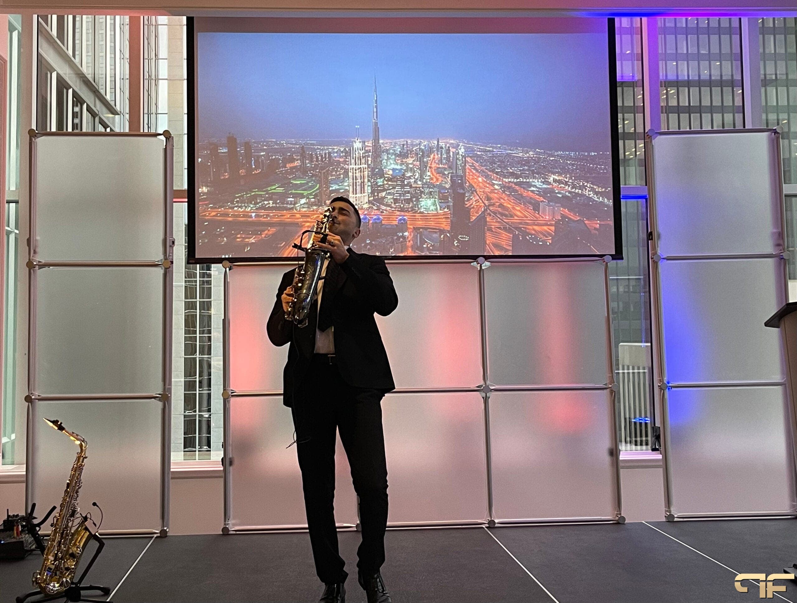 Saxophonist on stage before a Dubai night-skyline projection and frosted panels