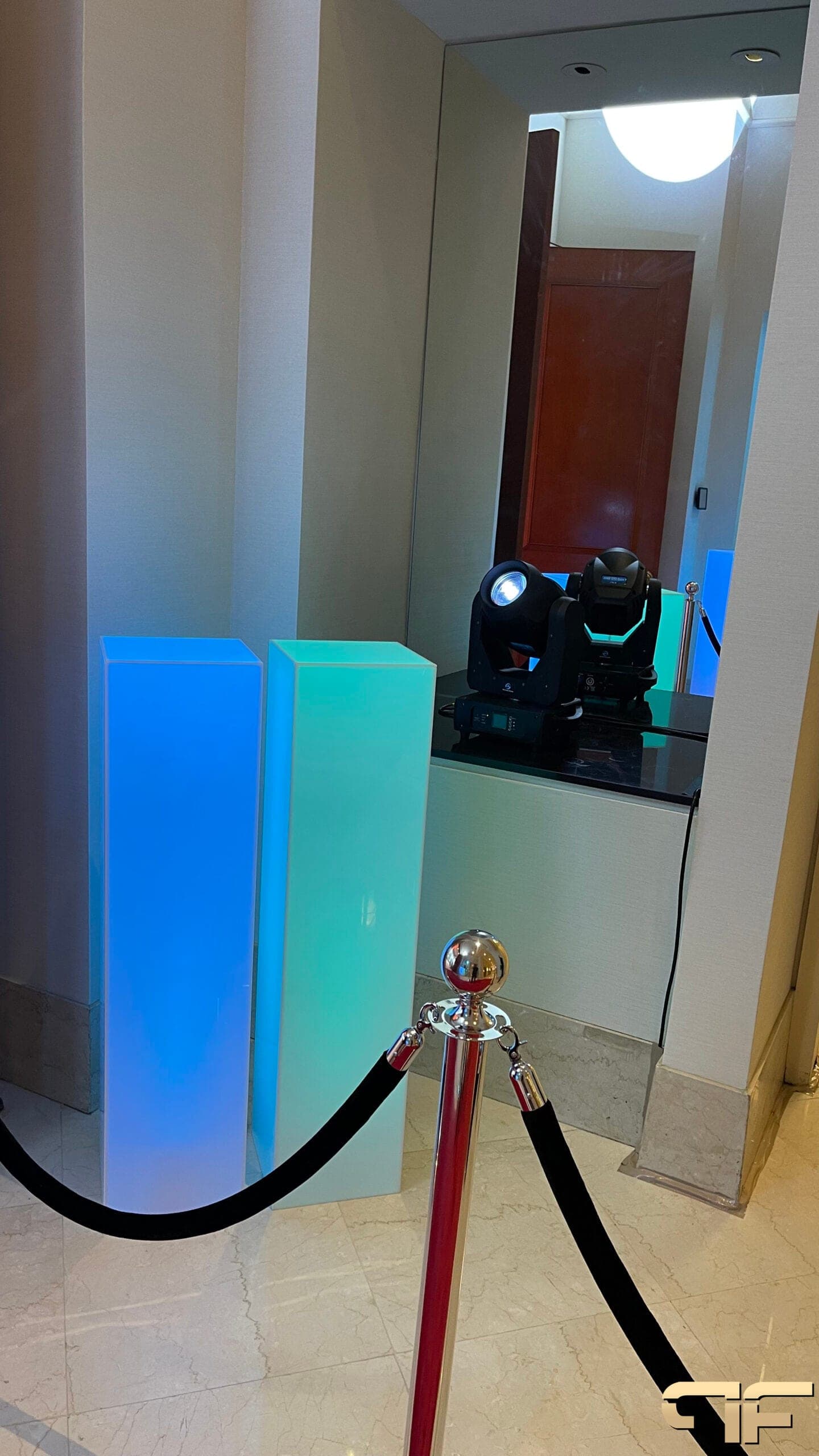 Two moving-head lights on a ledge beside blue and aqua LED plinths at the entrance