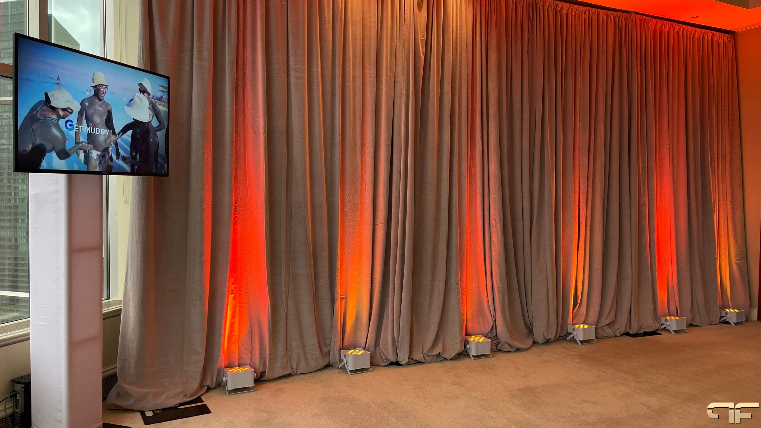 Taupe drape wall with amber uplights and a TV totem playing destination video