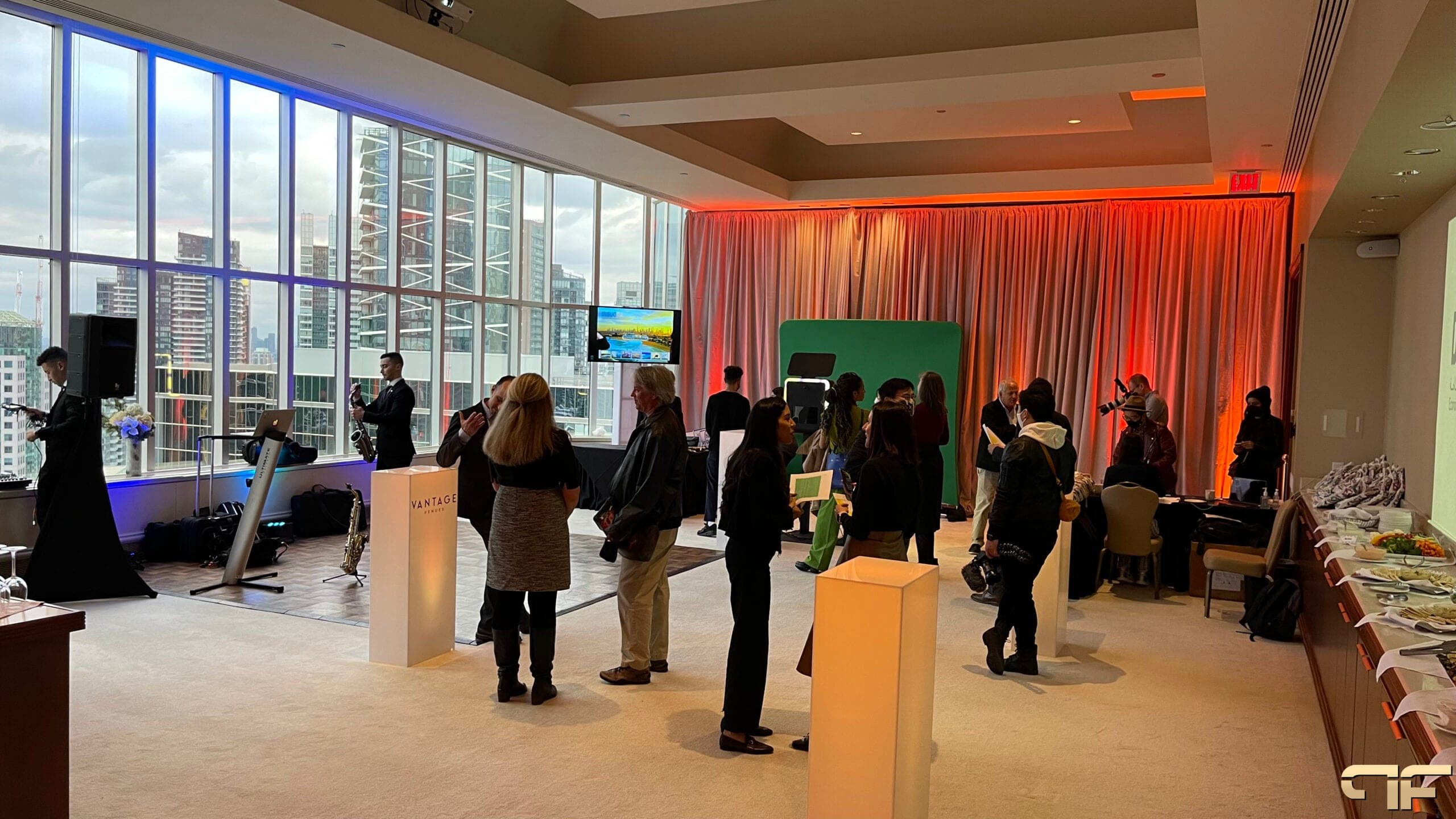 Guests mingling at the tourism reception, saxophonist by windows, orange-lit drape wall