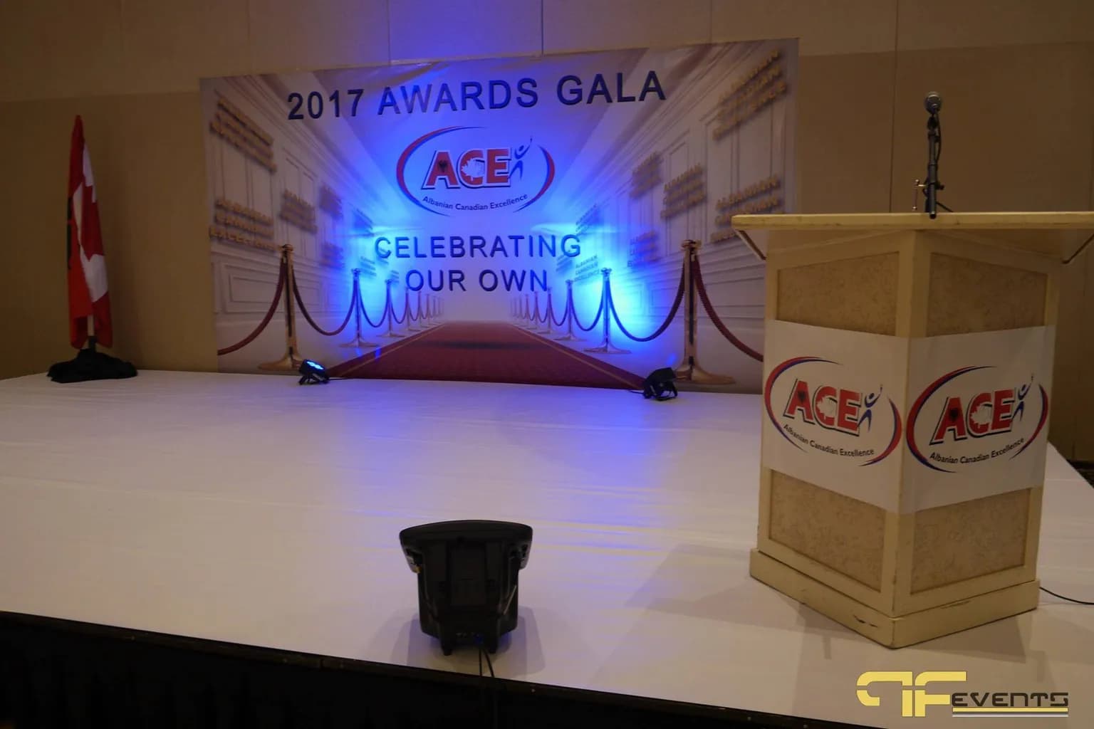Awards ceremony stage with a printed backdrop, blue uplighting, and a branded lectern with a microphone