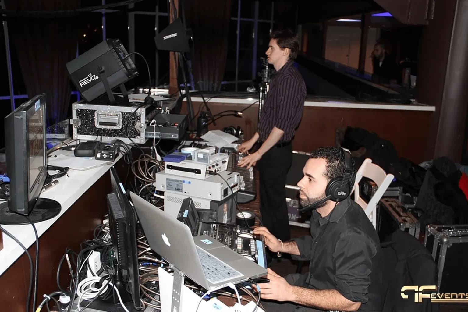 Audio and video technicians operating mixing consoles, monitors, and playback equipment at the back of a gala ballroom