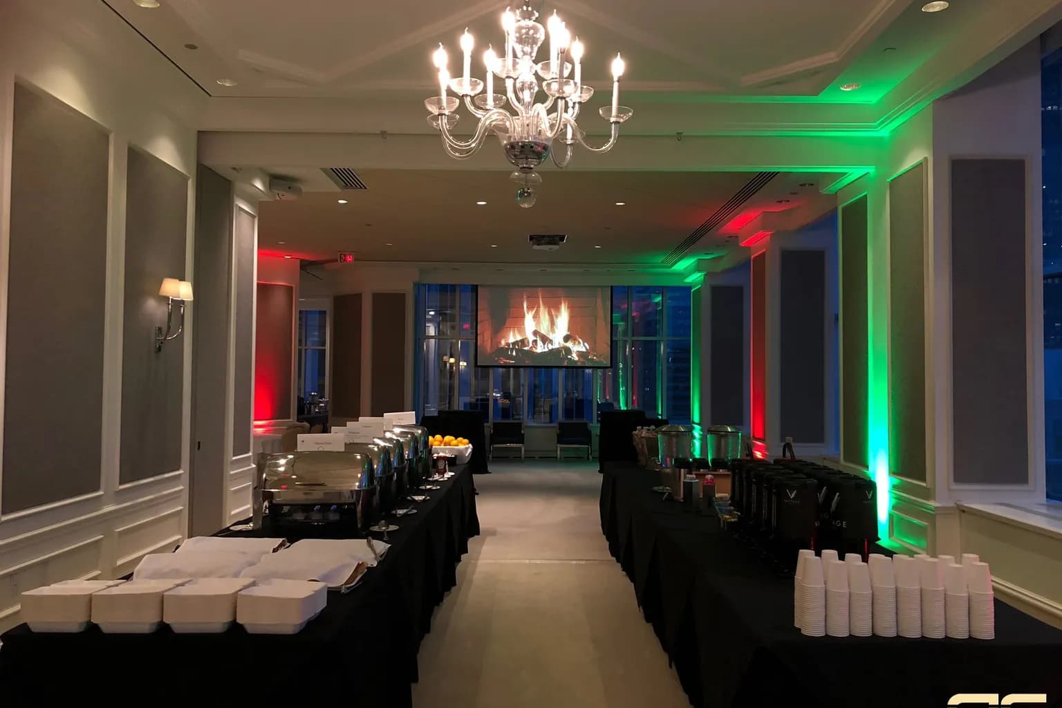 Holiday party room with red and green uplighting, a chandelier, and a fireplace video on the screen