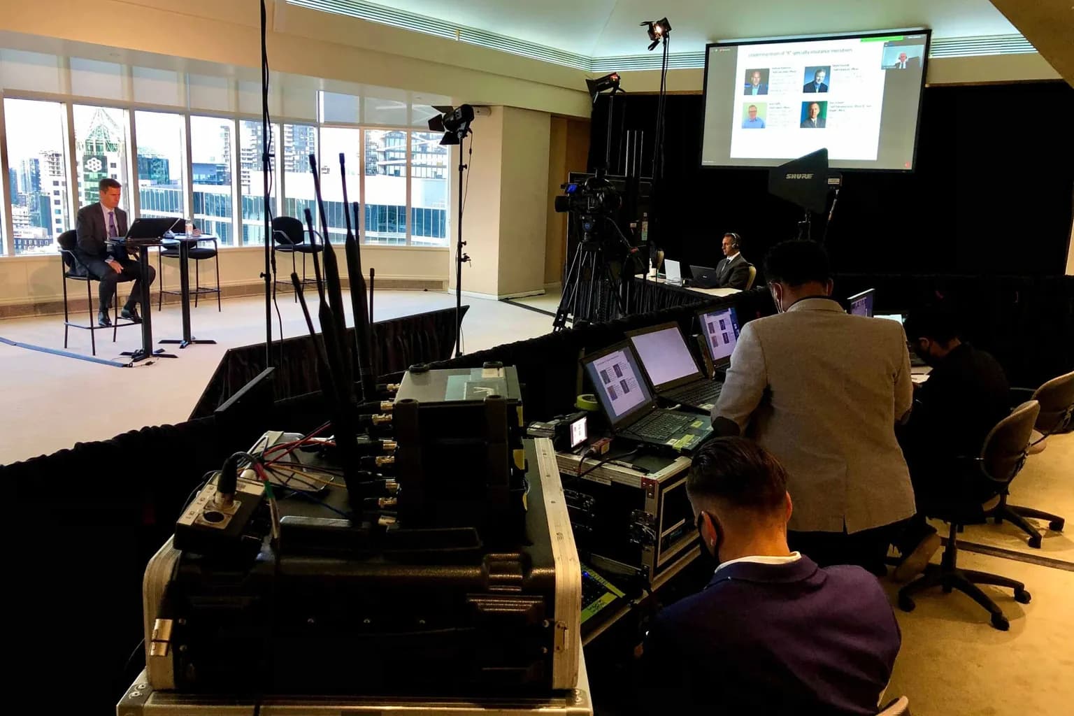 Hybrid event with a projection screen behind the speakers, cameras on tripods, and the control position in the foreground