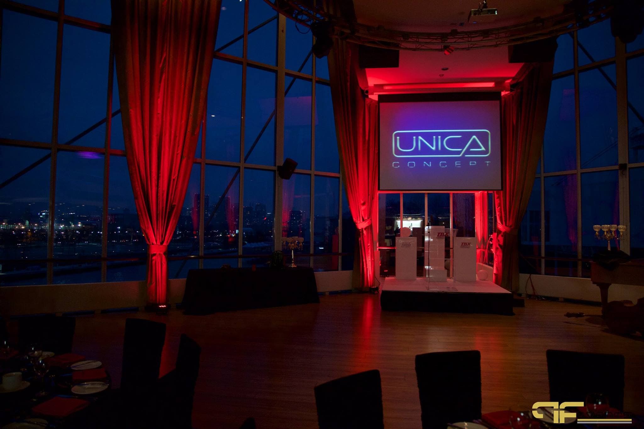 Screen showing Unica Concept logo above a riser, red uplit drapes and night skyline windows