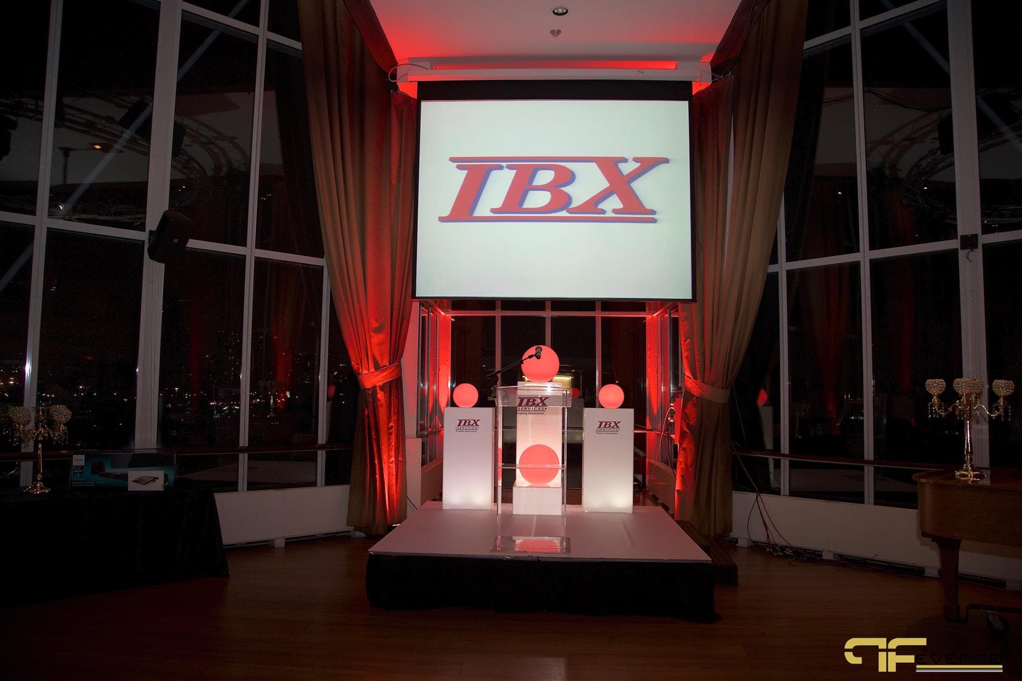 IBX logo on screen above acrylic podium, branded white plinths and glowing red spheres