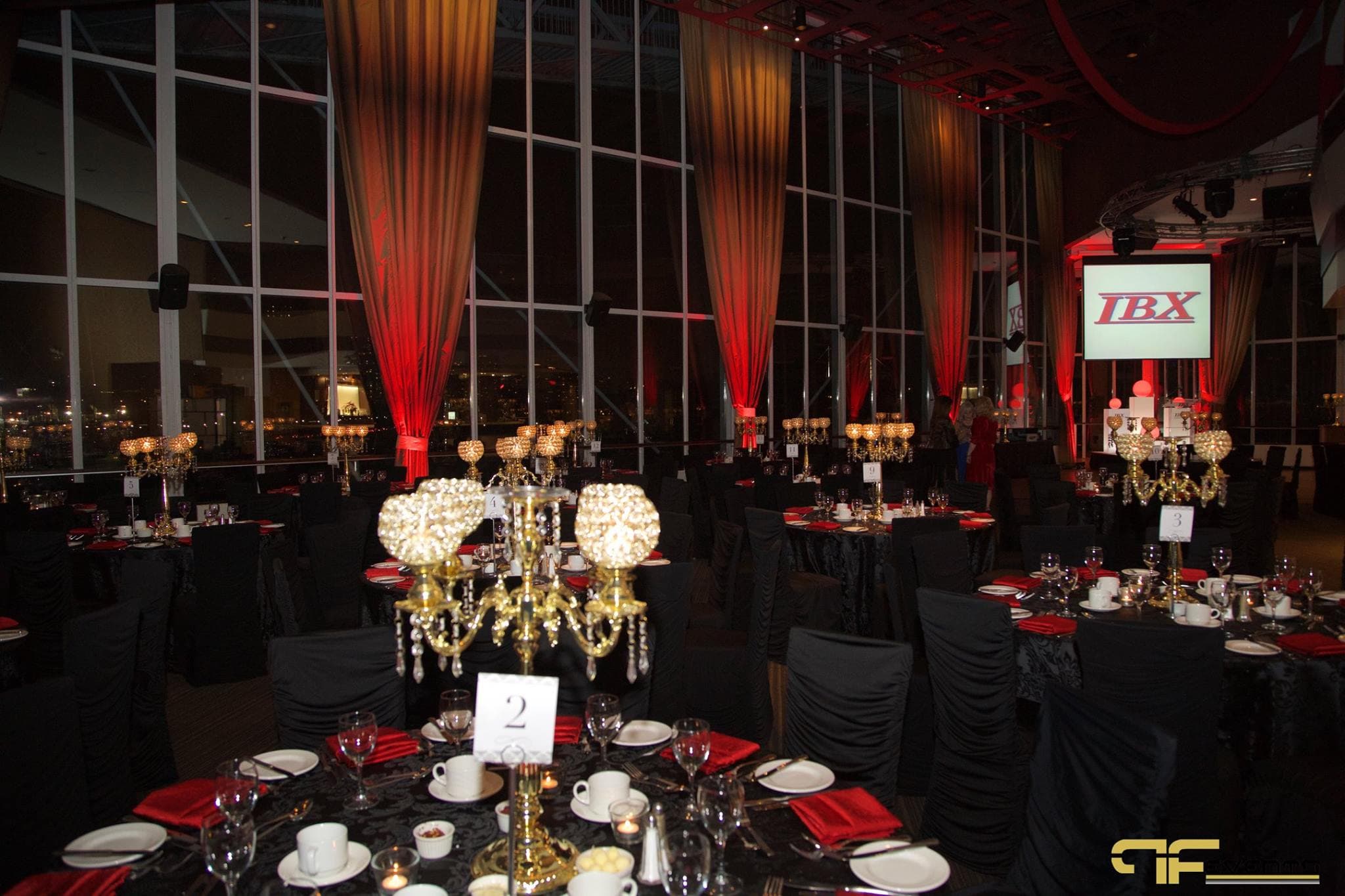 Dinner rounds with black linens, red napkins, gold candelabras; IBX screen at far end