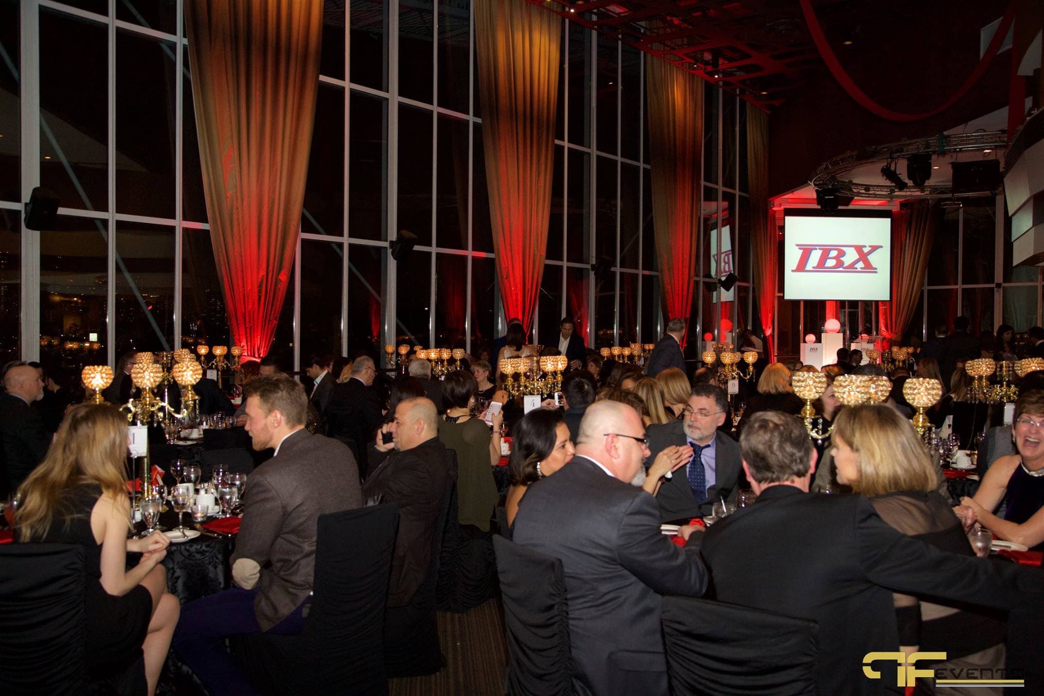 Guests seated at rounds in the glass pavilion, IBX logo on the screen behind