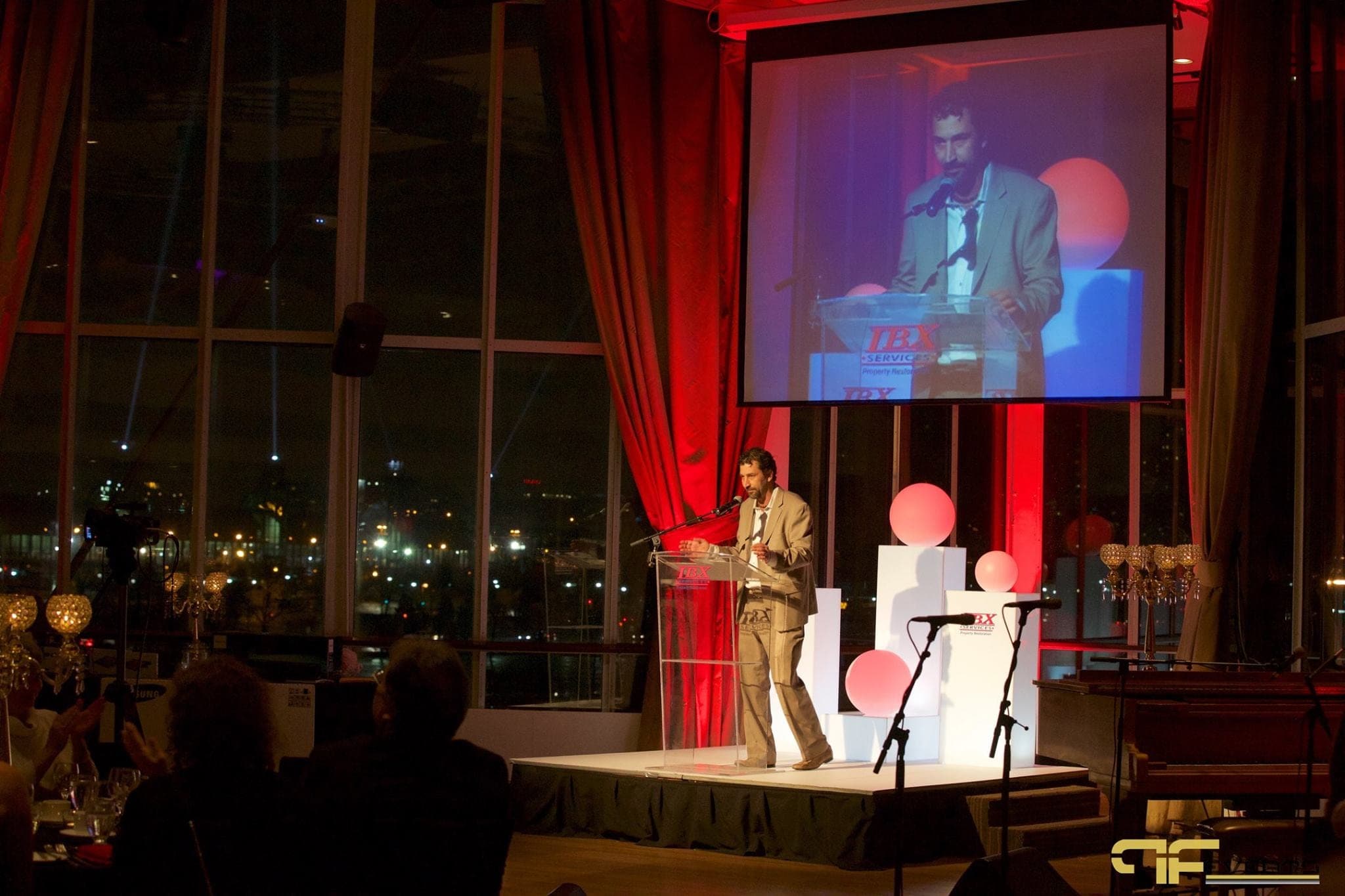 Speaker at IBX podium shown live on the screen above the stage, red drapes around