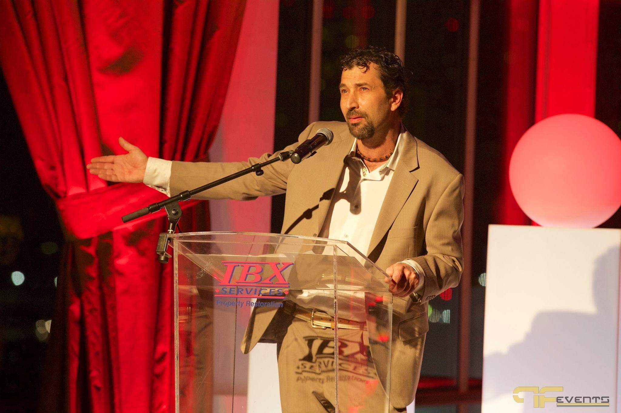 Speaker at the IBX Services podium gesturing toward red satin drape