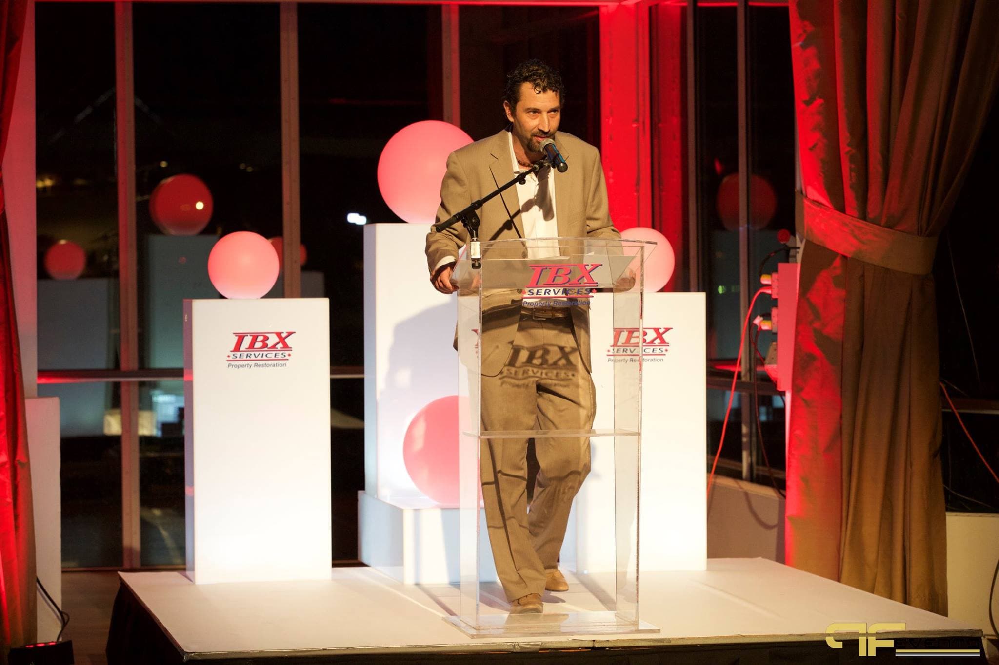 Speaker at acrylic IBX podium on white riser flanked by branded lit plinths