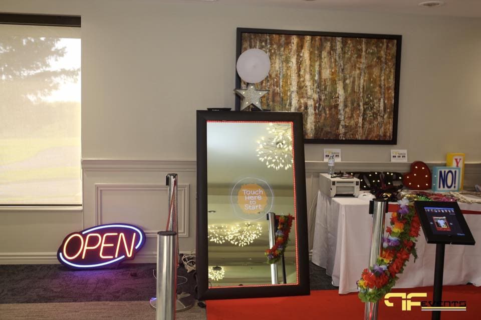 Magic-mirror photo booth with neon OPEN sign, stanchions and prop table
