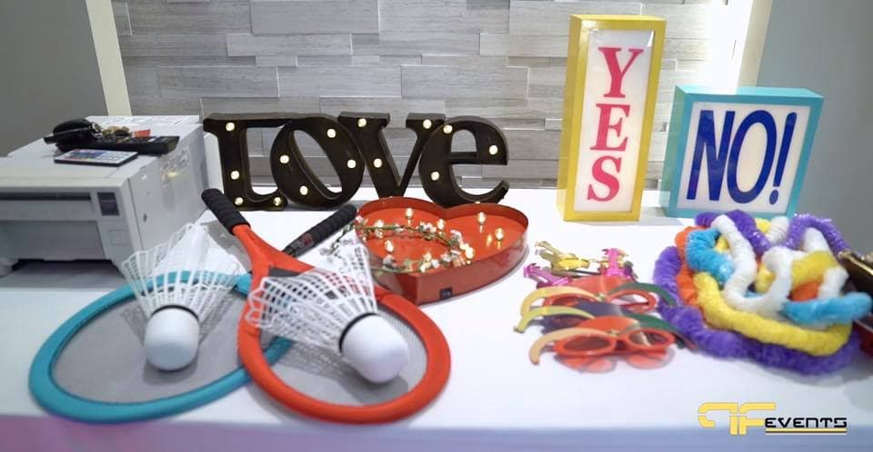 Photo booth props: marquee LOVE sign, YES/NO signs, rackets and leis