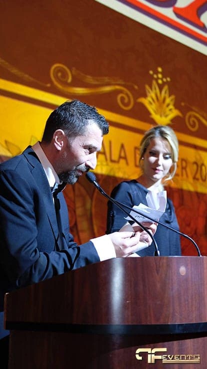 Presenter reading at the podium in front of the projected gala banner