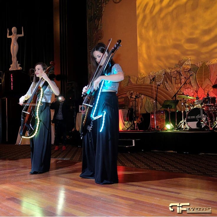 LED-lit electric cello duo on the dance floor in front of the band stage and mural