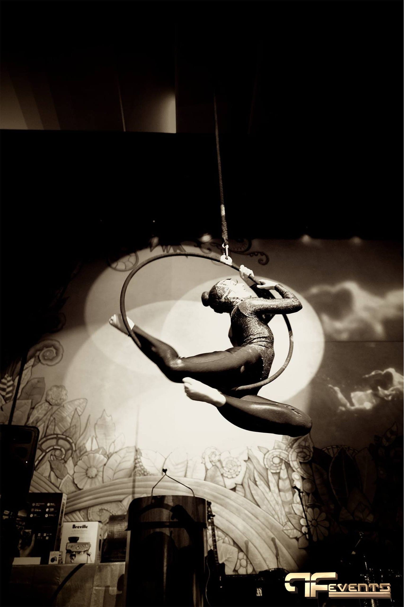 Aerial hoop performer spotlit against the floral stage mural, sepia tone