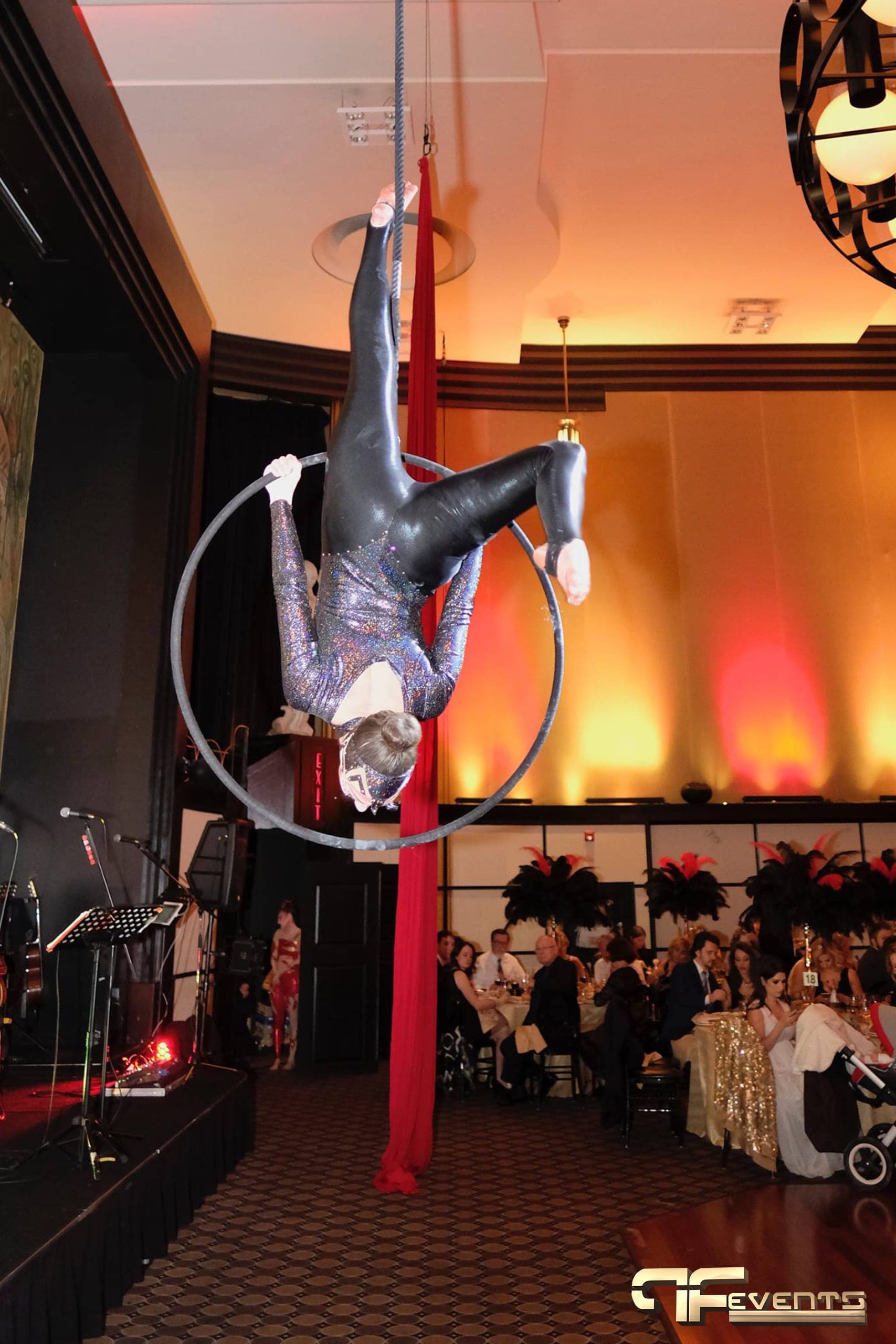 Aerialist on a hoop above the dance floor with red silks and amber-lit gala tables