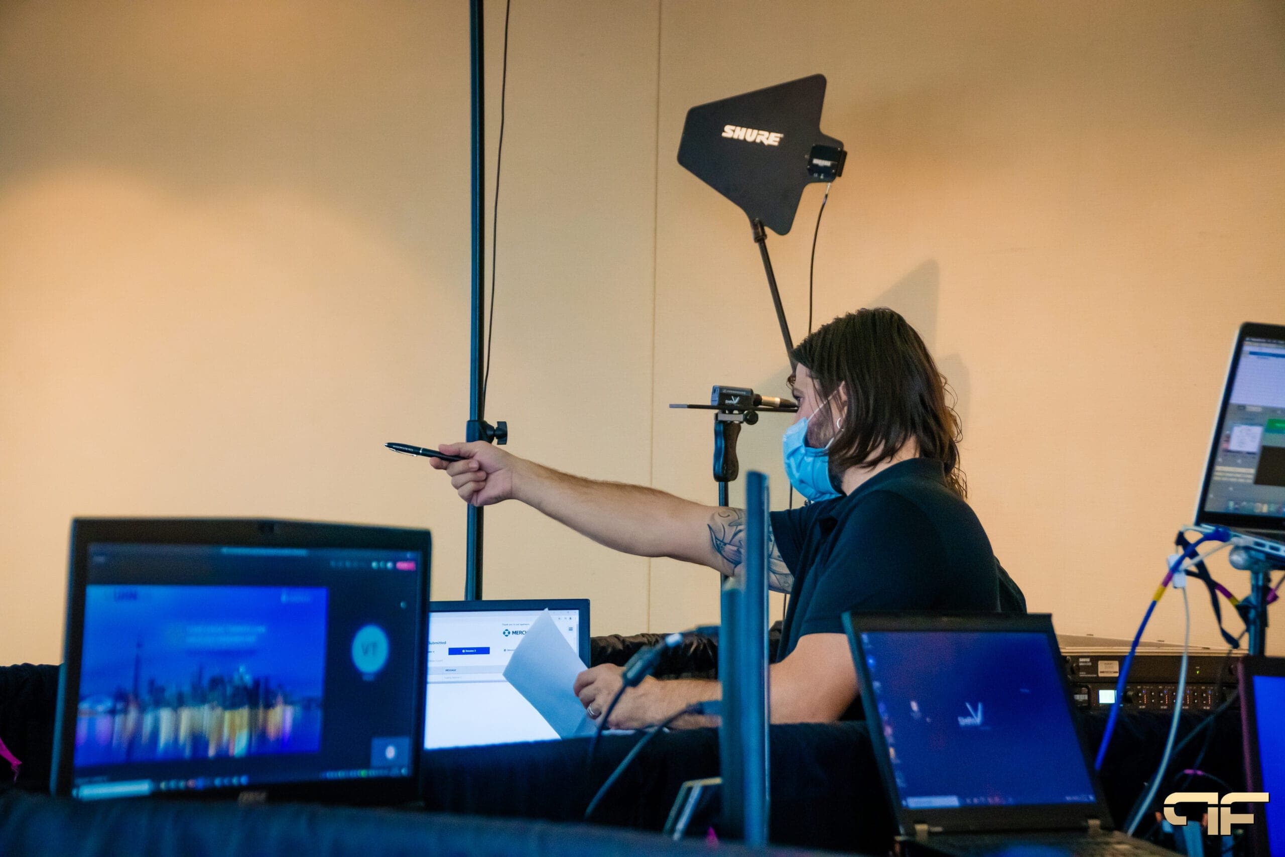 Masked technician cueing from laptops beside a Shure antenna