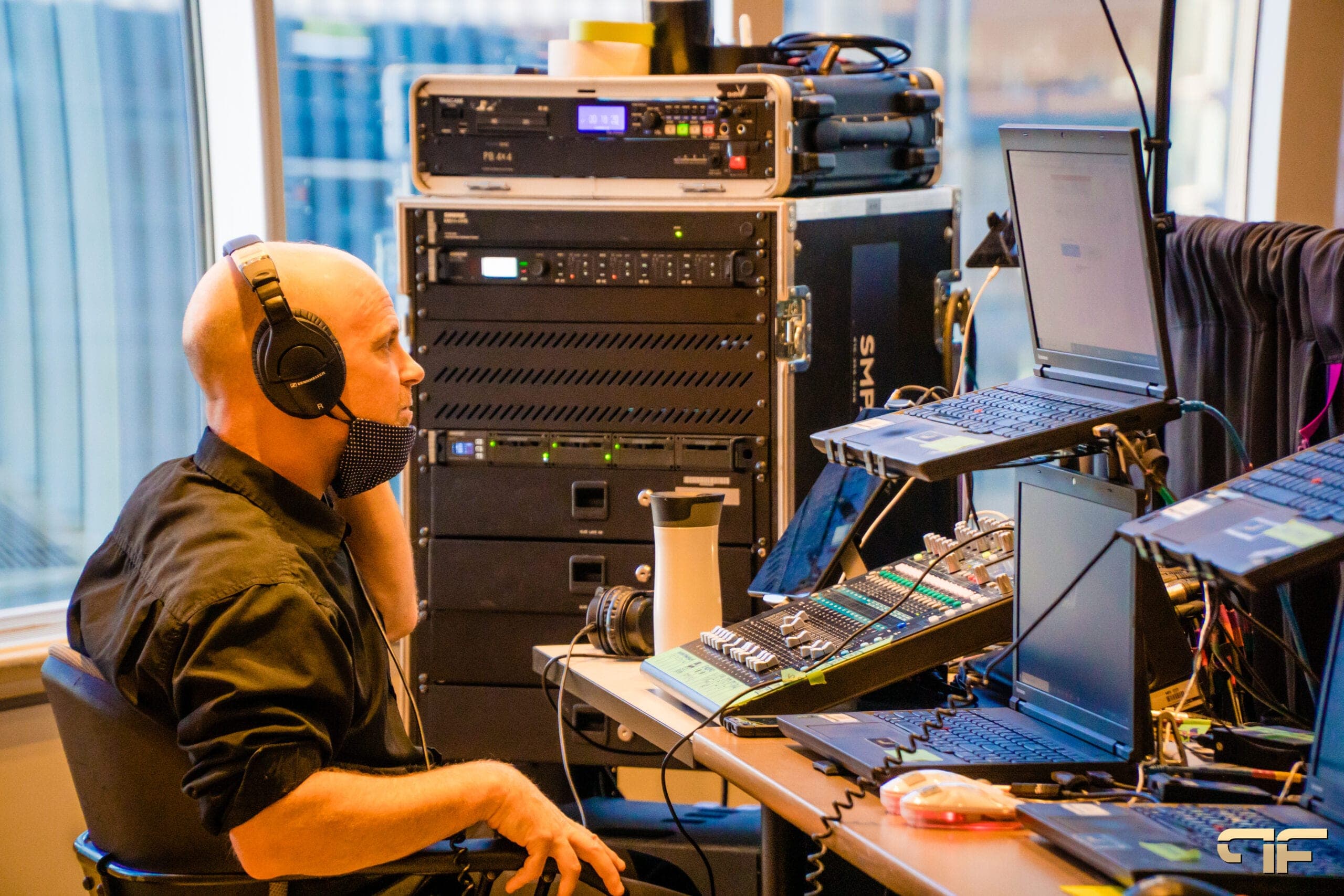 Audio engineer in headphones beside an equipment rack and digital mixer
