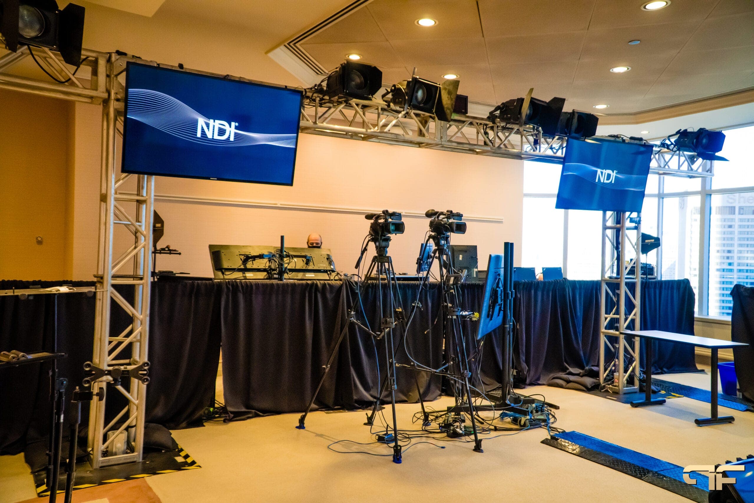 Hybrid broadcast set with truss lighting, two cameras and NDI screens