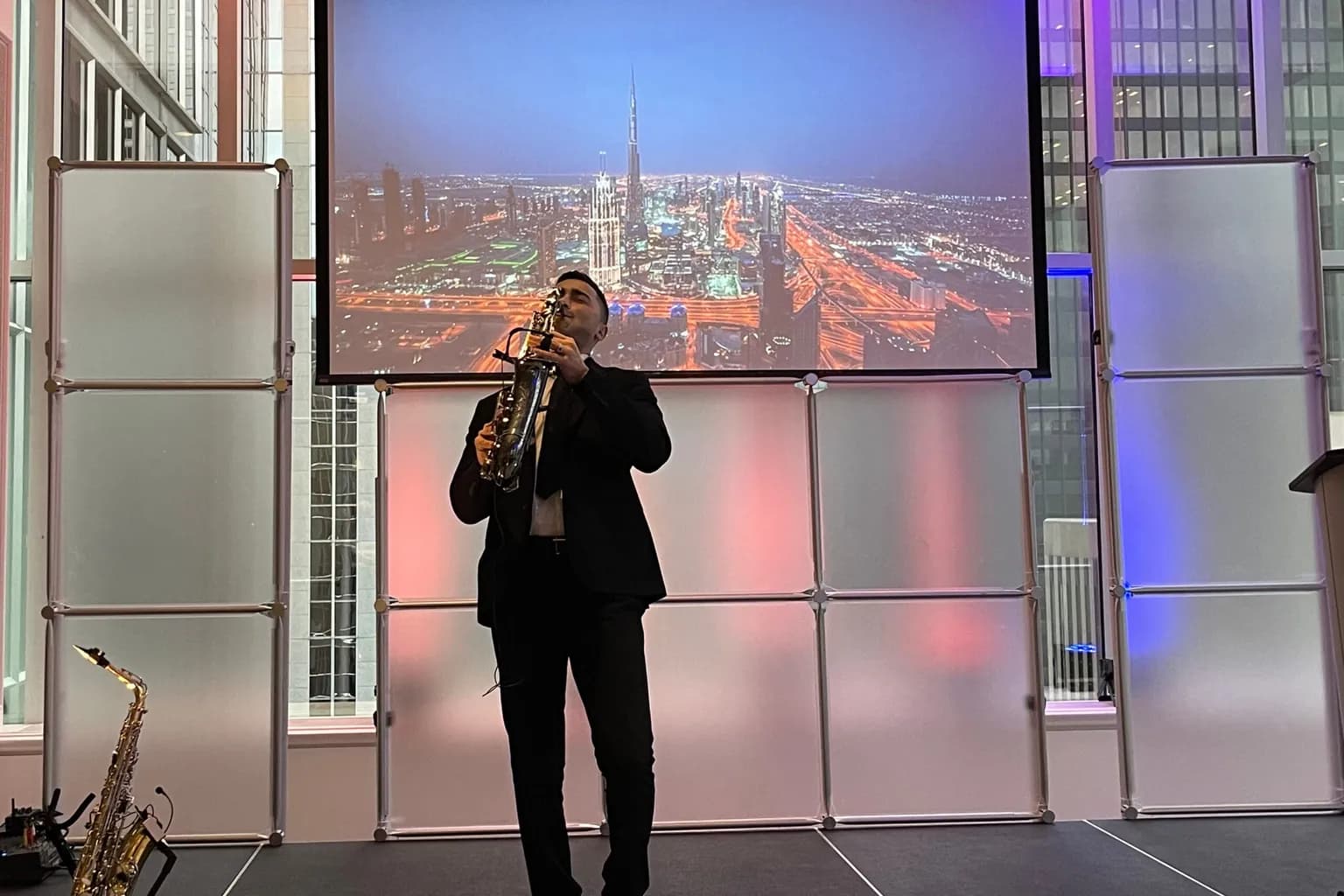Presenter on a stage with a large projection screen behind and side uplighting